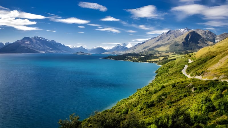 Landschaft mit türkisfarbenem See, schneebedeckten Bergen und grünen Hügeln nahe der Kerikeri High School.