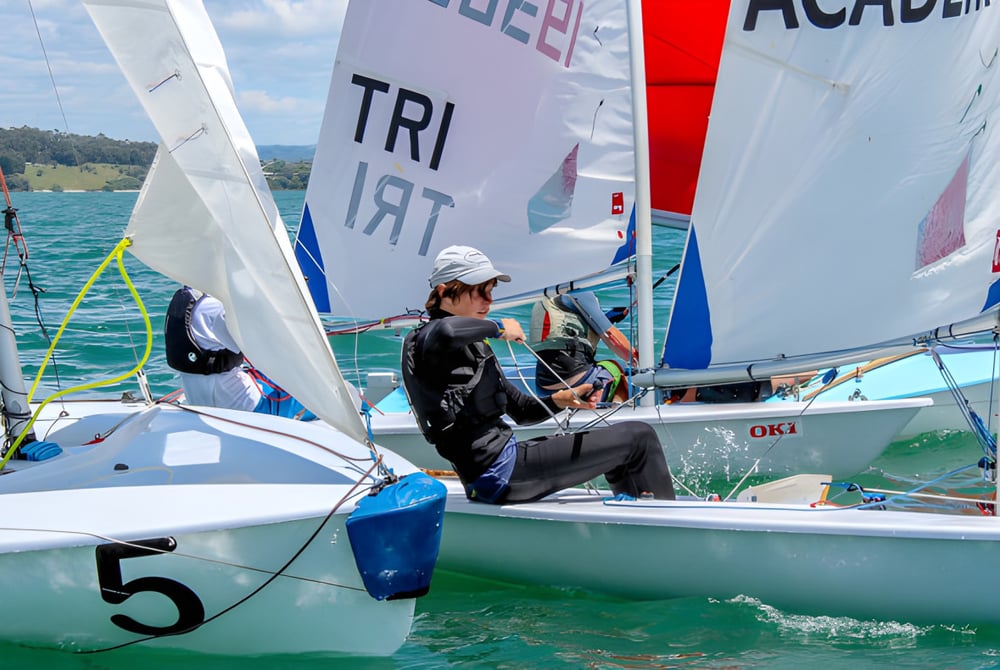 Ein Segelboot mit bunten Segeln auf dem Wasser vor Bergen liegt auf dem Gelände der Kerikeri High School.