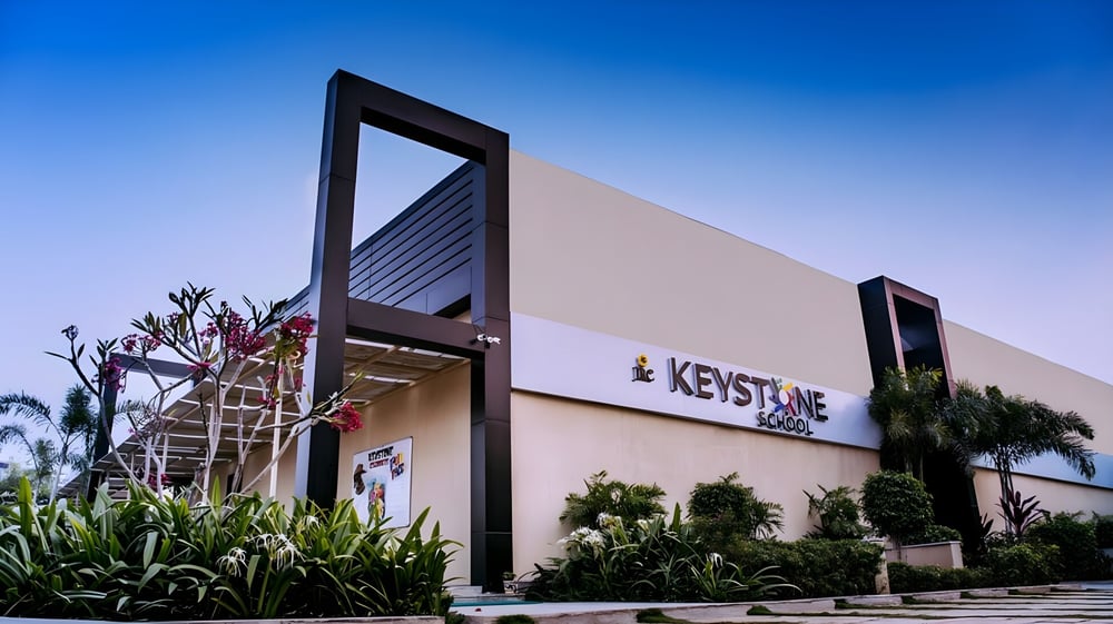 Das moderne Gebäude der Keystone School ist vor einem blauen Himmel und umgeben von grüner Vegetation zu sehen.