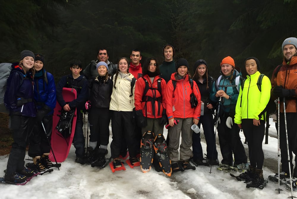 Eine Gruppe von Schülerinnen und Schülern der Keystone School steht in bunter Winterkleidung in einem verschneiten Wald.