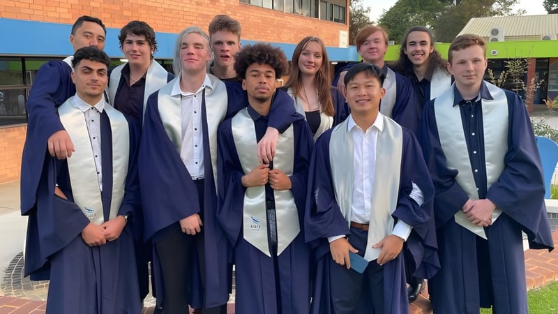 Eine Gruppe von Schülerinnen und Schülern des Kiara College steht in ihren Abschlussroben vor einem Backsteingebäude.