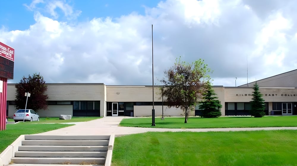 Das mehrstöckige moderne Schulgebäude von Kildonan East Collegiate mit Rasenfläche und Bäumen im Vordergrund unter bewölktem Himmel.