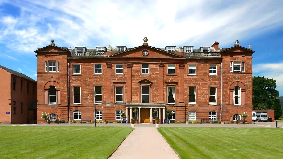 Das rotsteinige Hauptgebäude der Kilgraston School steht vor einem gepflegten Rasen unter blauem Himmel.