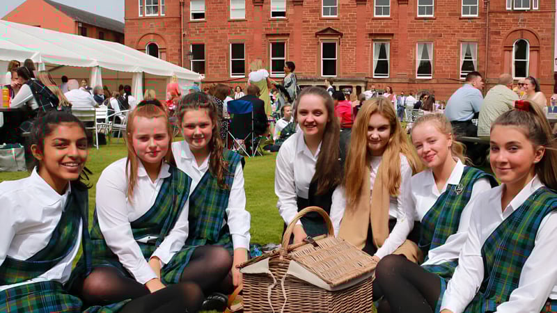Eine Gruppe Schülerinnen der Kilgraston School trägt traditionelle schottische Kleidung vor einem Zeltbereich mit weiteren Menschen.