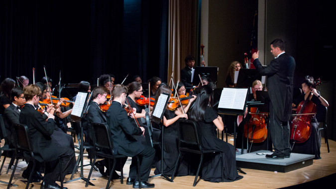 Ein großes Orchester spielt auf der Bühne unter der Leitung eines Dirigenten an der Kilkenny City Vocational School.