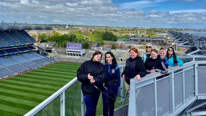 Eine Gruppe von Schülerinnen und Schülern der Kilkenny City Vocational School steht auf einem Balkon mit Blick auf ein großes Sportstadion und die Stadt im Hintergrund.
