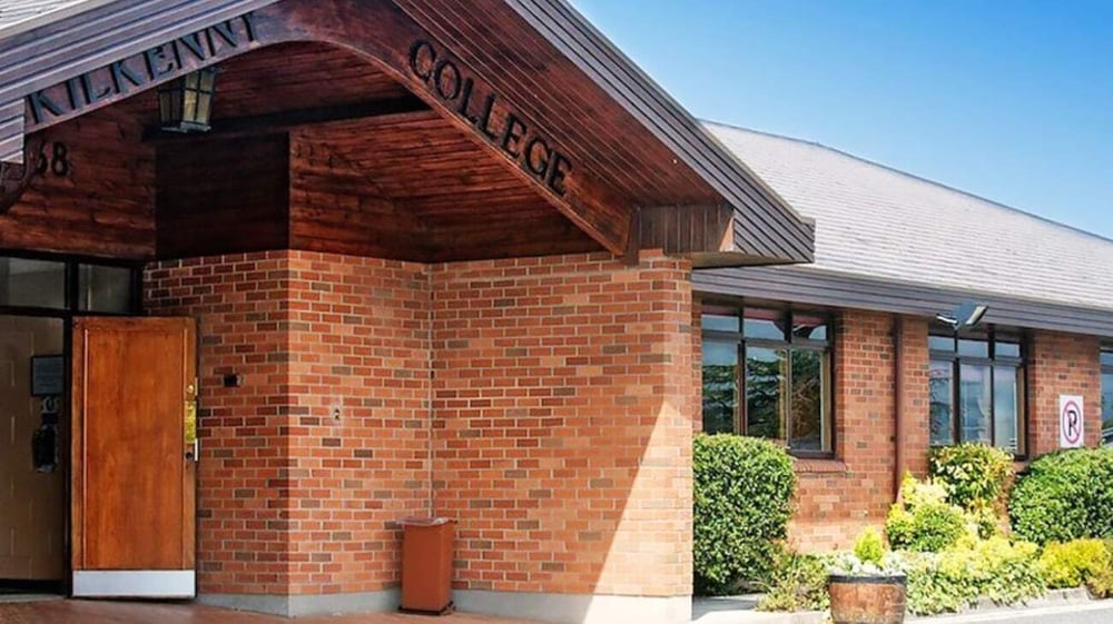 Das Gebäude mit hölzernem Eingang und einem Schild der Atl Clinic steht auf dem Gelände des Kilkenny College, umgeben von grüner Bepflanzung.