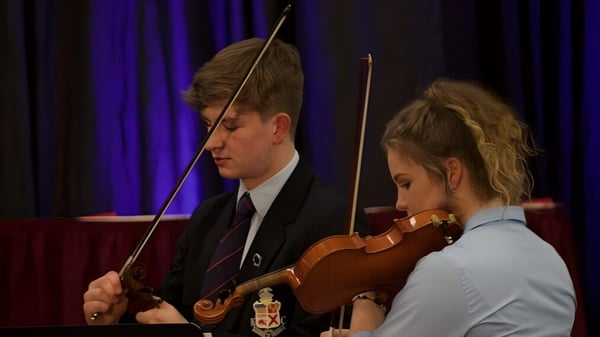 Zwei Schüler des Kilkenny College führen gemeinsam mit Geige und Bogen auf einer Bühne mit rotem Vorhang auf.