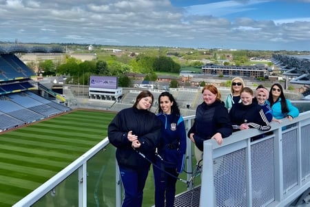 Schüler der Kilkenny City Vocational School stehen auf einem Balkon mit Blick auf ein großes Sportstadion und die Stadt im Hintergrund.