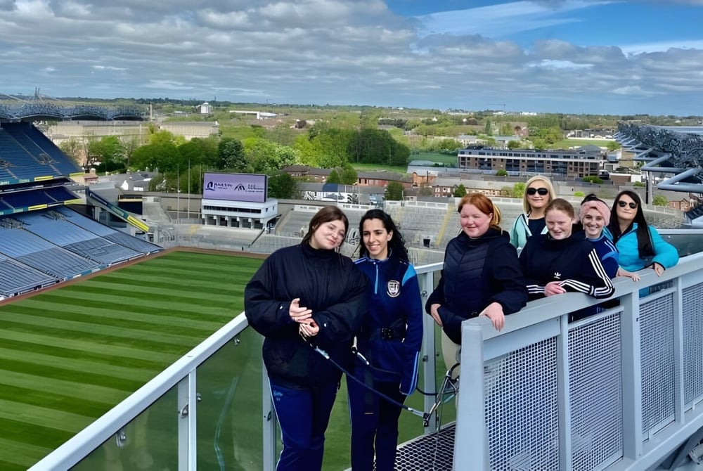 Schüler der Kilkenny City Vocational School stehen auf einem Balkon mit Blick auf ein großes Sportstadion und die Stadt im Hintergrund.