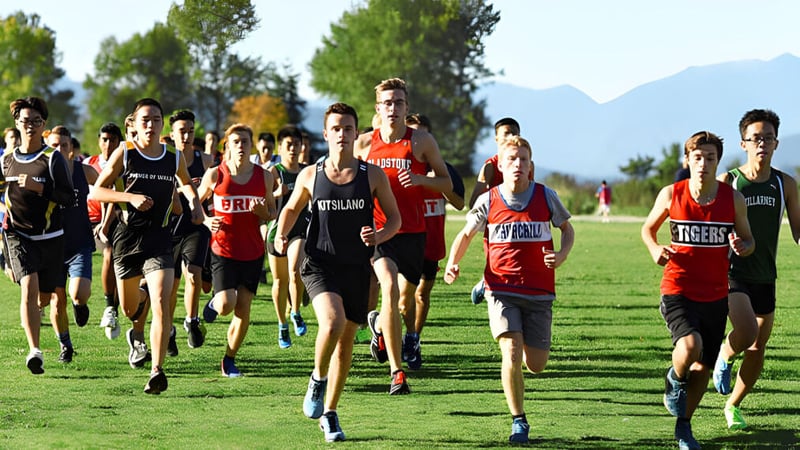 Schüler der Killarney Secondary School nehmen an einem Crosslauf auf einem Feld mit Bäumen und Bergen teil.
