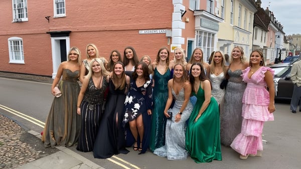 Eine Gruppe junger Frauen in Abendkleidern posiert auf der Straße vor bunten Häusern auf dem Campus der Kimbolton School.