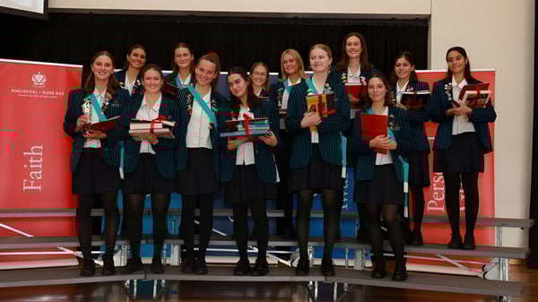 Eine Gruppe von Absolventinnen der Kincoppal-Rose Bay steht vor einem roten Hintergrund mit Urkunden in der Hand.