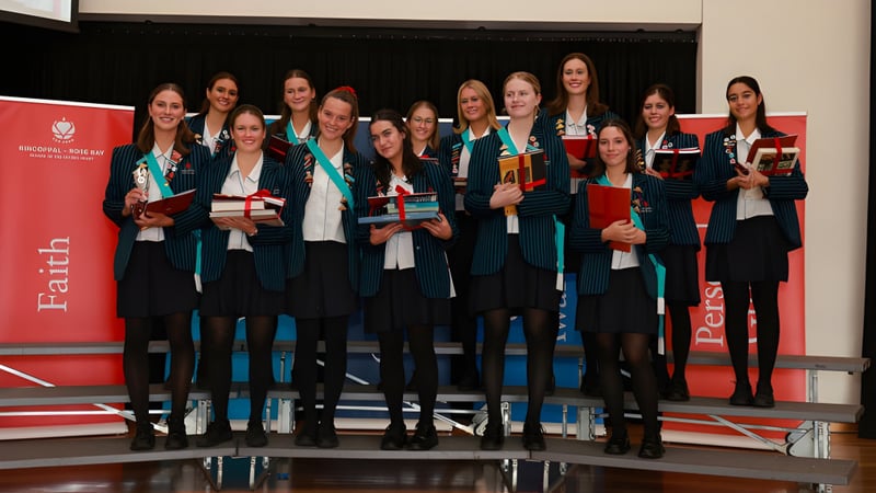 Eine Gruppe von Absolventinnen der Kincoppal-Rose Bay steht vor einem roten Hintergrund mit Urkunden in der Hand.