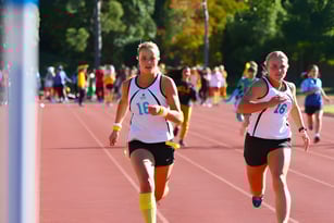 Zwei Athletinnen laufen auf der Laufbahn auf dem Gelände von Kincoppal-Rose Bay vor Zuschauern und Bäumen.