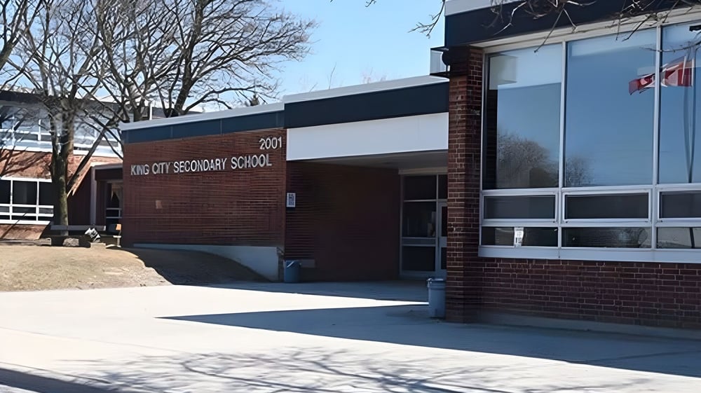 Das Backsteingebäude der King City Secondary School ist von Bäumen umgeben und ein gepflasterter Weg führt zum Eingang.