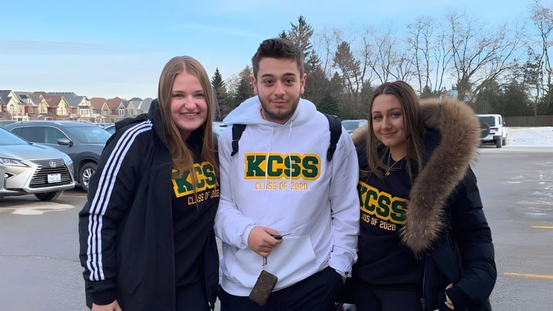 Drei Schüler stehen gemeinsam im Außenbereich der King City Secondary School mit Wohnhäusern im Hintergrund.