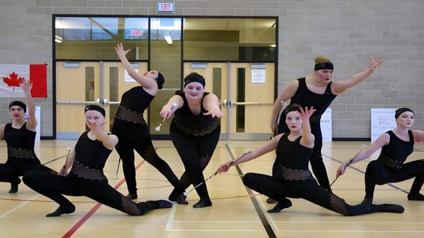 Eine Tanzgruppe der King City Secondary School führt eine synchronisierte Choreografie vor einer Backsteinwand im Innenraum auf.