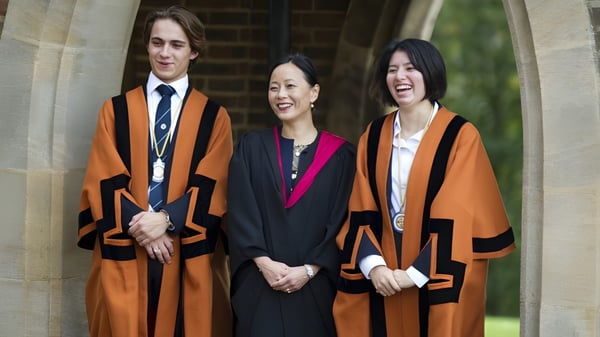 Drei Personen in akademischen Roben stehen vor einem steinernen Bogen auf dem Gelände der King Edward's Witley School.