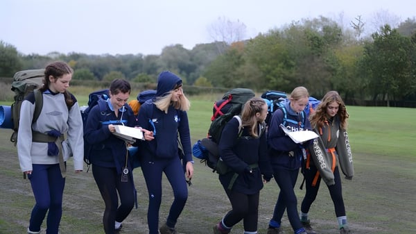Eine Gruppe von Schülerinnen und Schülern der King Edward's Witley School versammelt sich auf einem Grasfeld inmitten von Bäumen.