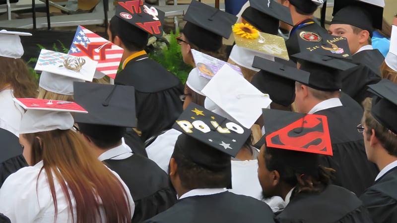 Absolventen des King William's College tragen schwarze Talare und Mützen bei einer Abschlussfeier im Freien.