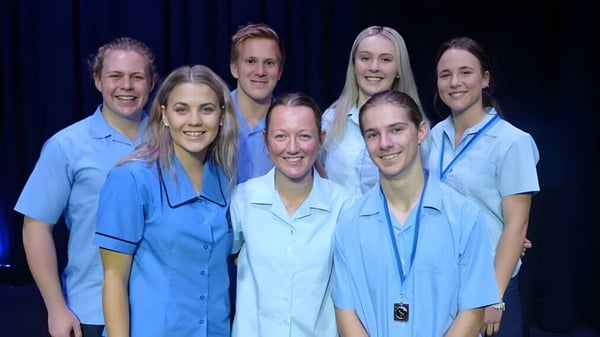Eine Gruppe von Schülerinnen und Schülern der Kingaroy State High School trägt blaue Uniformen und steht vor dunklem Hintergrund.
