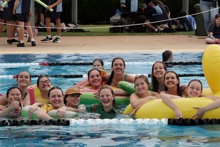 Eine Gruppe Schülerinnen der Kingaroy State High School versammelt sich in einem Schwimmbad vor Zuschauern und einem Volleyballnetz.
