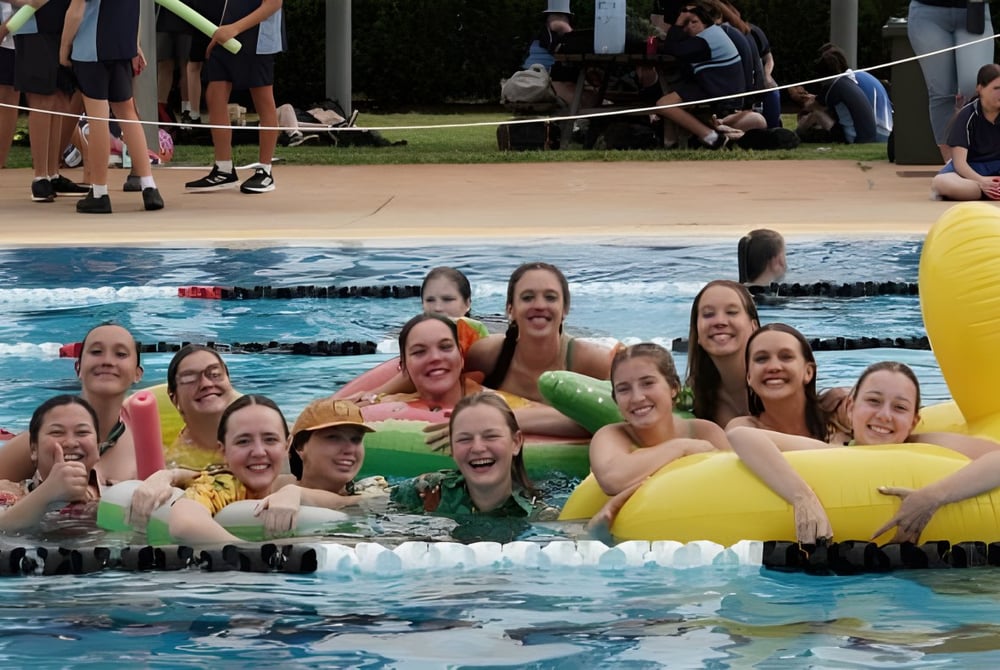 Eine Gruppe Schülerinnen der Kingaroy State High School versammelt sich in einem Schwimmbad vor Zuschauern und einem Volleyballnetz.