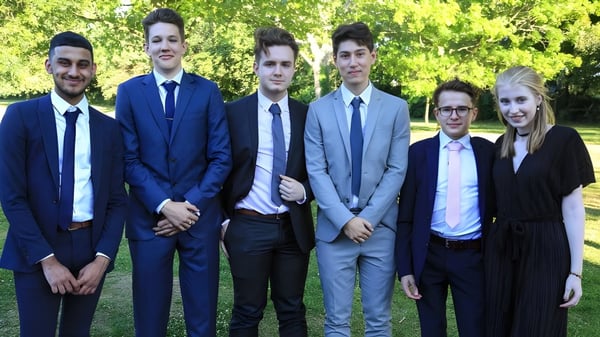 Eine Gruppe von sechs Personen in formeller Kleidung steht zusammen im Park auf dem Gelände der Kingham Hill School.