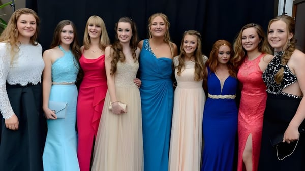 Eine Gruppe junger Frauen in festlichen Kleidern posiert gemeinsam vor einem dunklen Hintergrund auf dem Campus der King's Bruton.