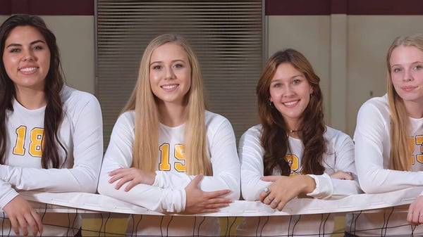 Vier Schülerinnen der Kings Christian School in weißen Trikots mit der Zahl 13 stehen gemeinsam in einer Sportumgebung vor einem Metallzaun.