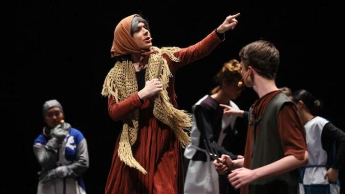 Eine Frau in rotem Gewand und Kopftuch gestikuliert im Vordergrund auf dem Campus des King's College.