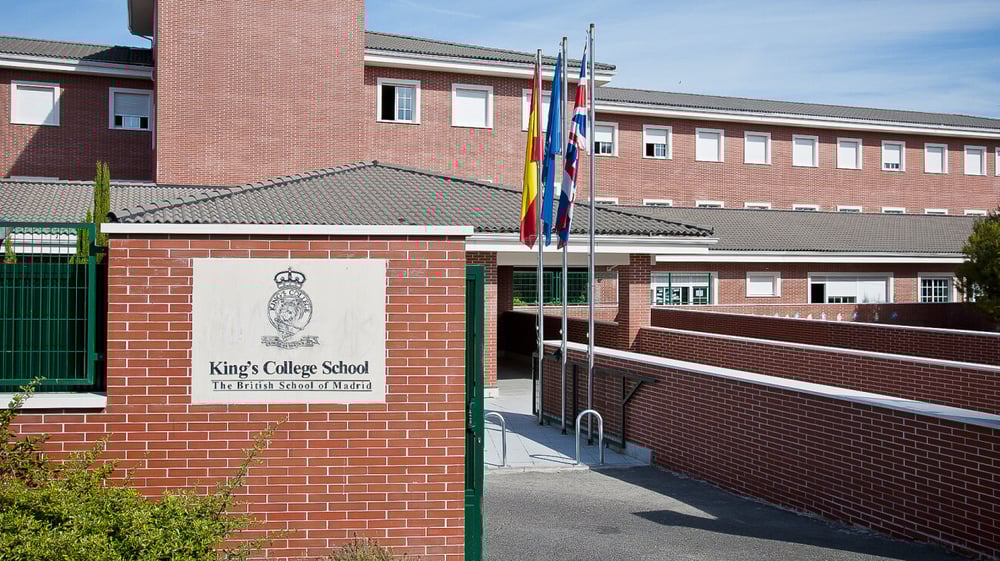 Das Backsteingebäude mit dem Schriftzug King's College ist von einem grünen Zaun umgeben und mehrere Flaggen wehen im Hintergrund.