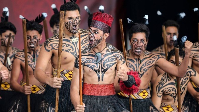 Eine Gruppe mit Körperbemalung und traditioneller Kleidung steht gemeinsam im dunklen Raum auf dem Campus des King's College.