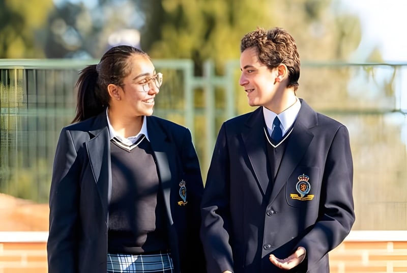 Zwei Schülerinnen und Schüler in Schuluniformen unterhalten sich auf dem Außengelände des King's College.