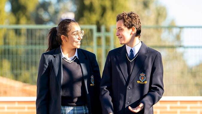 Zwei Schüler des King’s College stehen im Schulhof zusammen und unterhalten sich vor einem Backsteinhaus mit Bäumen.