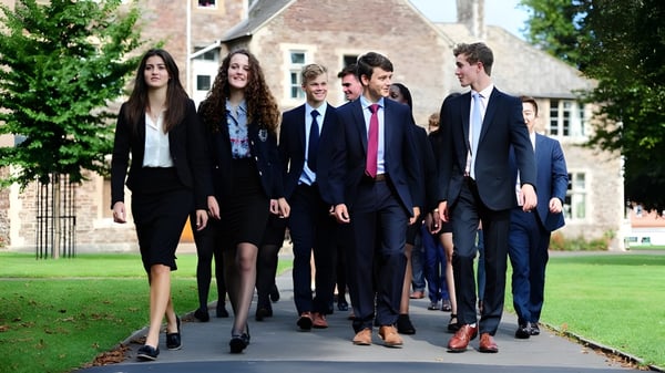 Eine Gruppe Schülerinnen und Schüler des King’s College geht auf einem Weg zwischen grünen Büschen nahe einem historischen Gebäude.