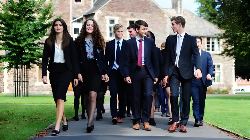 Eine Gruppe Schülerinnen und Schüler des King’s College geht auf einem Weg zwischen grünen Büschen nahe einem historischen Gebäude.