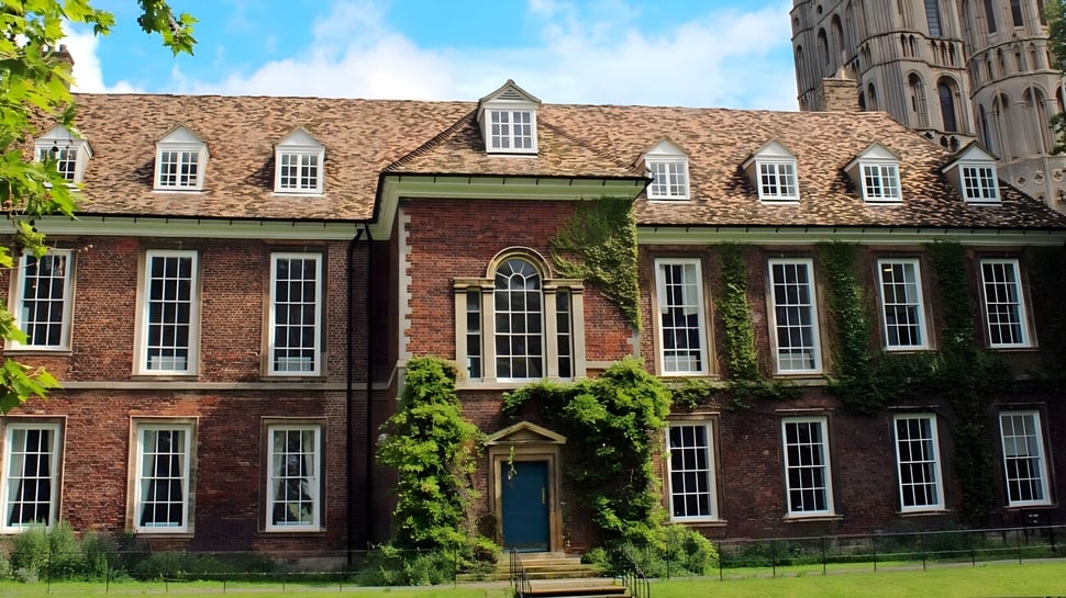 Das historische Backsteingebäude mit Ziegeldach auf dem Campus von King's Ely ist von grüner Vegetation umgeben.