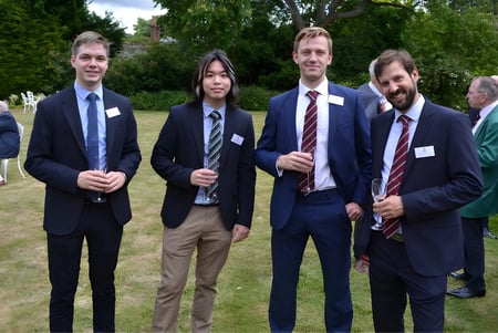 Vier Männer in formeller Kleidung stehen gemeinsam auf einer Wiese auf dem Gelände der King's School.