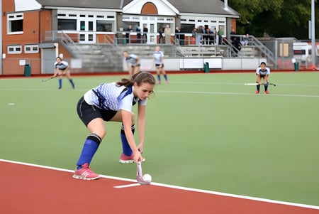 Eine Schülerin oder ein Schüler der King's School Rochester ist in Sportkleidung auf dem Sportfeld in einer Hockposition zu sehen.