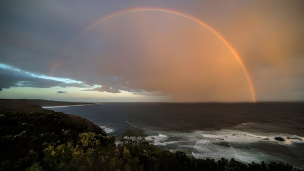 Ein Regenbogen spannt sich über die Küstenlandschaft neben der Kingscliff High School mit rauen Felsen und Vegetation.