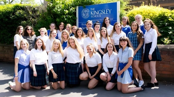 Eine Gruppe Schülerinnen posiert vor dem Schild der Kingsley School umgeben von Bäumen und Grünflächen.