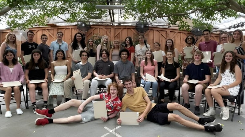 Eine Gruppe von Schülerinnen der Kingsville District High School versammelt sich im Freien vor einer Holzstruktur und grüner Vegetation.