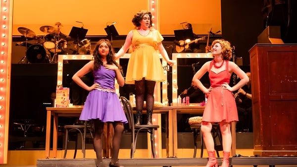 Drei Schülerinnen der Kingswood Oxford treten auf der Bühne mit einer Band im Hintergrund auf.