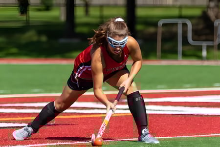 Eine Schülerin von Kingswood Oxford ist in Sportkleidung mit einem Hockeyschläger auf der Laufbahn in Bereitschaft.