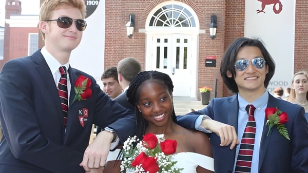 Drei Schülerinnen und Schüler der Kingswood Oxford School posieren in formeller Kleidung vor einem Backsteingebäude mit gewölbtem Eingang.