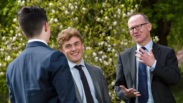 Drei Männer in Anzügen führen ein Gespräch vor grünem Hintergrund auf dem Gelände der Kingswood School.