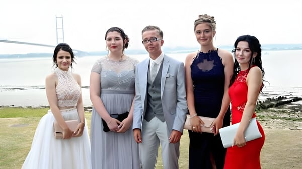 Eine Gruppe elegant gekleideter Personen posiert im Freien vor einer Wasser- und Landschaftskulisse auf dem Gelände der Kingswood School.