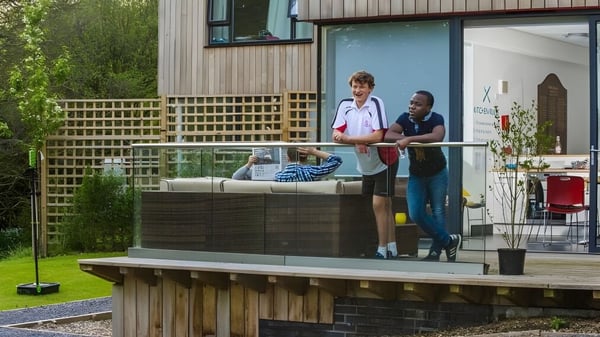 Zwei Personen stehen auf dem Holzdeck der Kingswood School vor einem Holzzaun und grüner Bepflanzung.